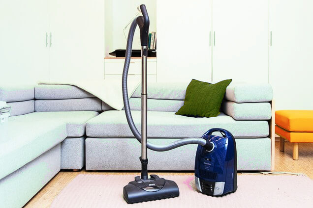 blue color canister vacuum cleaner in the living room on the carpet with sofa set