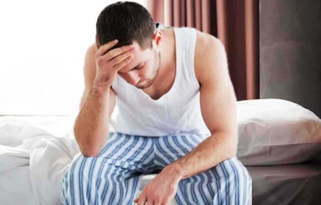 a man in pajamas sitting on a bed - disadvantages of masturbation